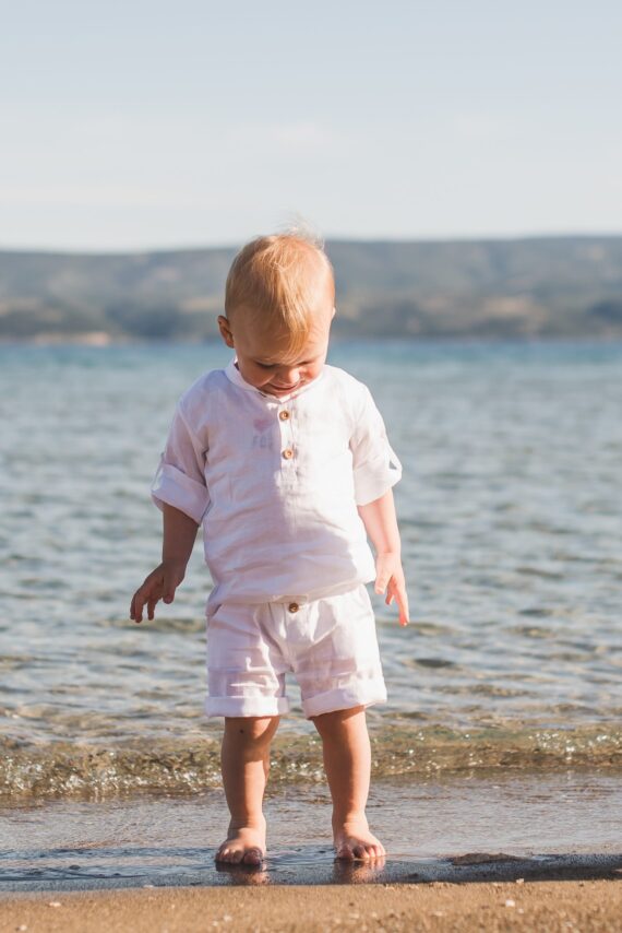 Dječak na plaži u odijelu od lana u bijeloj boji.